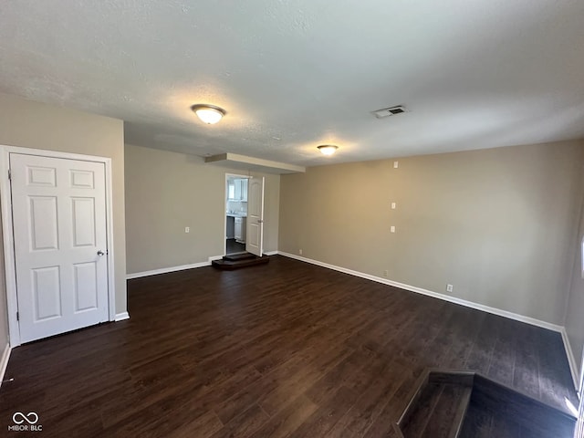 empty room featuring baseboards, dark wood-type flooring, a textured ceiling, and visible vents