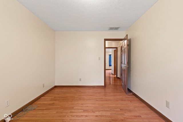 empty room featuring baseboards, visible vents, light wood-style flooring, and a textured ceiling