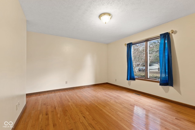 empty room with a textured ceiling, hardwood / wood-style flooring, visible vents, and baseboards