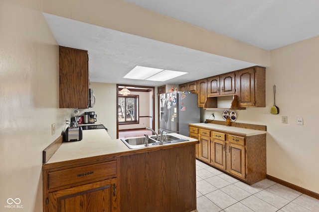 kitchen with a skylight, stainless steel appliances, light tile patterned flooring, a sink, and a peninsula