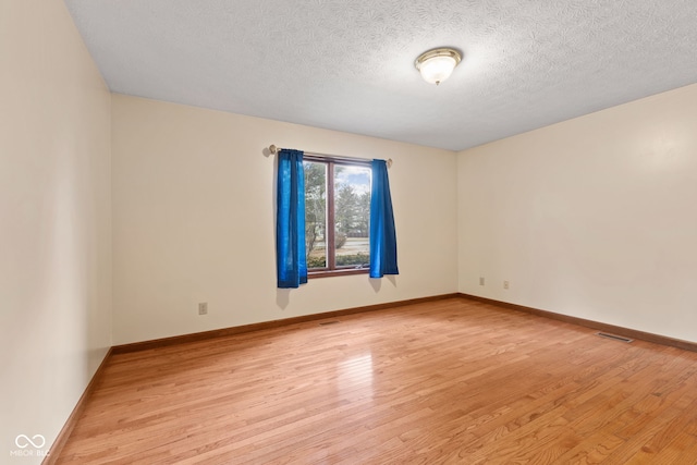 unfurnished room with light wood-type flooring, visible vents, a textured ceiling, and baseboards