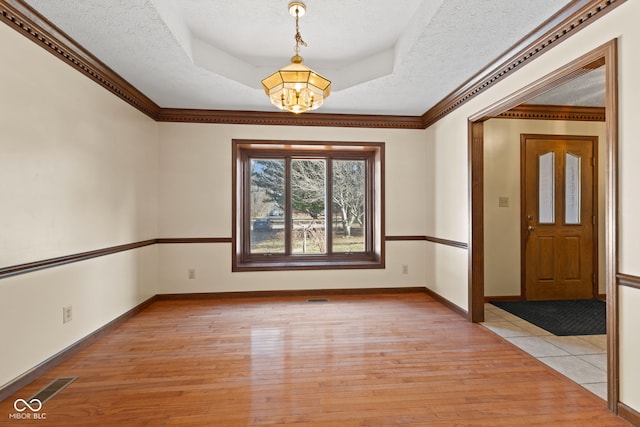 foyer with light wood-style floors, a tray ceiling, visible vents, and a textured ceiling