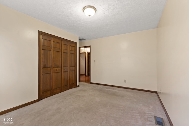 unfurnished bedroom with a textured ceiling, light colored carpet, visible vents, baseboards, and a closet