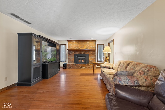 living area featuring a textured ceiling, wood finished floors, visible vents, baseboards, and a brick fireplace