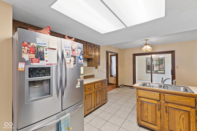 kitchen with brown cabinetry, stainless steel fridge with ice dispenser, decorative light fixtures, a sink, and light tile patterned flooring