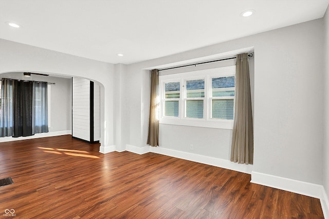 unfurnished room with baseboards, arched walkways, wood finished floors, and recessed lighting