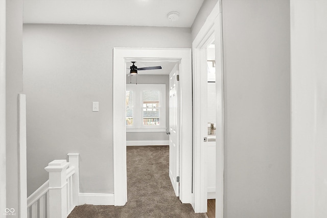 corridor with baseboards, dark colored carpet, and an upstairs landing