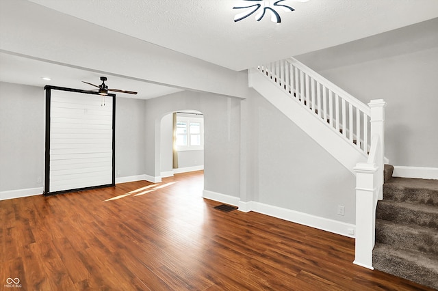 unfurnished living room with arched walkways, wood finished floors, a ceiling fan, baseboards, and stairs