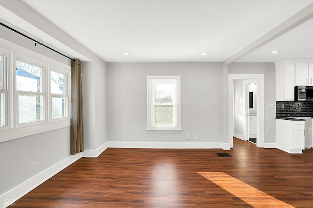 unfurnished living room featuring visible vents, dark wood-style flooring, a wealth of natural light, and baseboards