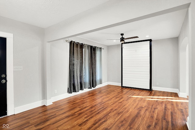 unfurnished bedroom featuring arched walkways, wood finished floors, a ceiling fan, and baseboards