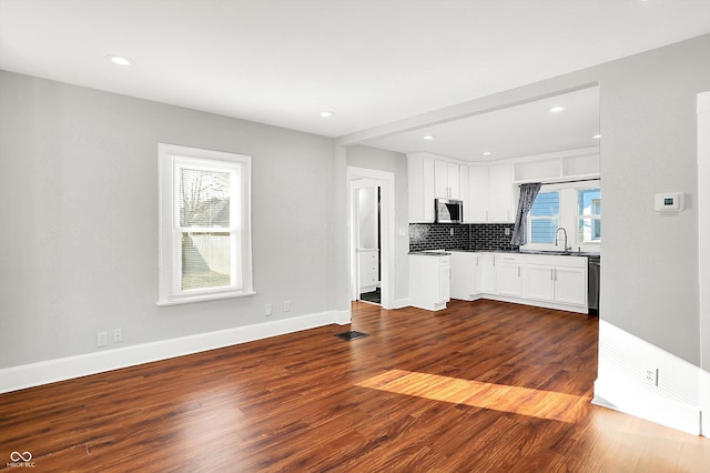 kitchen featuring baseboards, white cabinets, dark wood finished floors, decorative backsplash, and stainless steel microwave