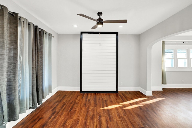 spare room featuring arched walkways, wood finished floors, and baseboards