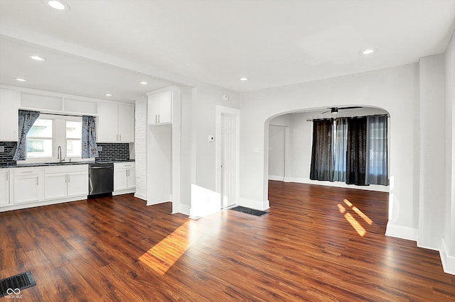 kitchen with dark wood-style floors, arched walkways, dark countertops, stainless steel dishwasher, and a sink