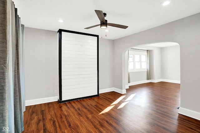 unfurnished bedroom featuring baseboards, arched walkways, wood finished floors, and recessed lighting