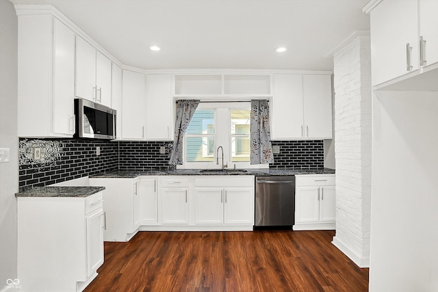 kitchen with stainless steel appliances, dark wood-style flooring, a sink, backsplash, and dark stone counters