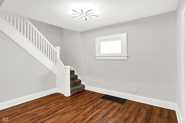 stairway featuring visible vents, a textured ceiling, baseboards, and wood finished floors