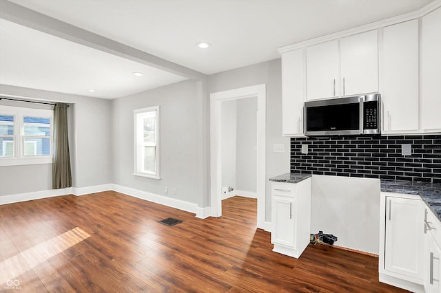 kitchen featuring dark wood-type flooring, stainless steel microwave, visible vents, and tasteful backsplash