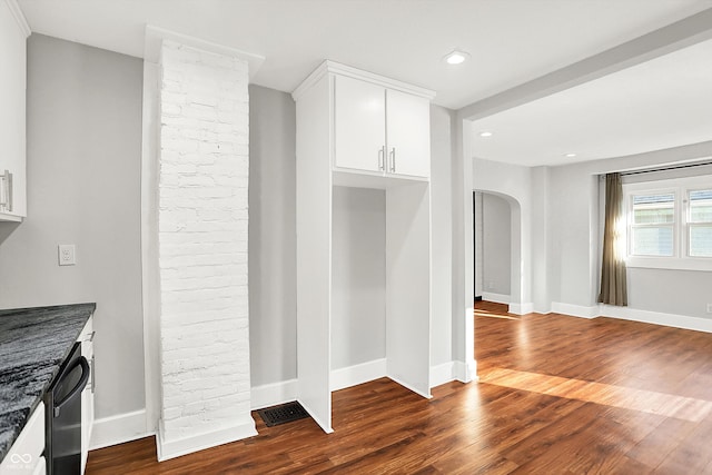 kitchen with dark wood-type flooring, arched walkways, white cabinetry, and baseboards