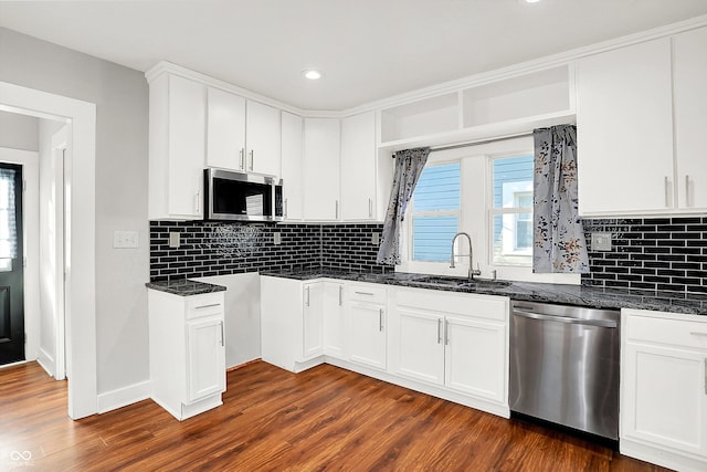 kitchen featuring dark wood-type flooring, dark stone countertops, stainless steel appliances, and a sink