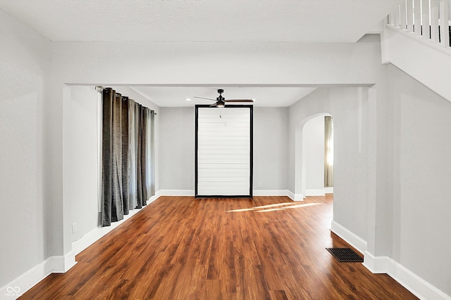 unfurnished room with baseboards, visible vents, a ceiling fan, arched walkways, and wood finished floors