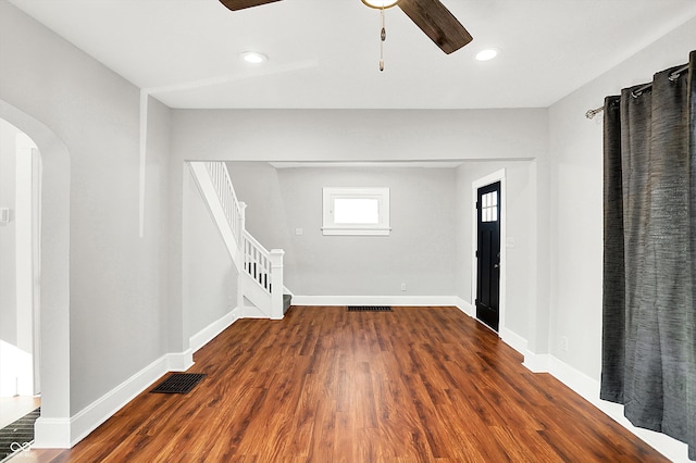 spare room with arched walkways, ceiling fan, wood finished floors, visible vents, and stairway