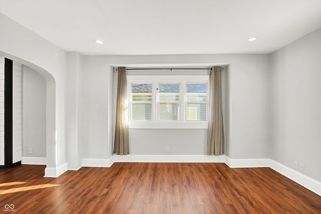 unfurnished room with baseboards, arched walkways, wood finished floors, and recessed lighting