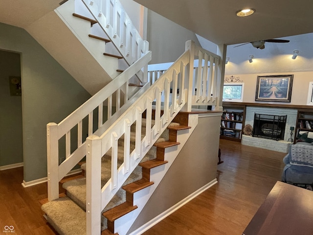 staircase featuring a fireplace, baseboards, a ceiling fan, and wood finished floors