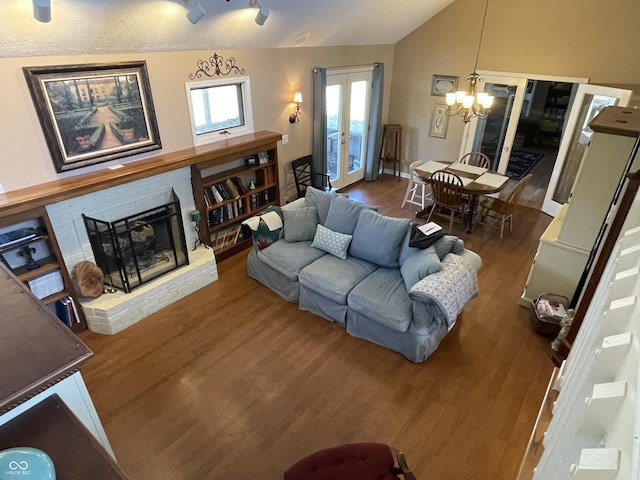 living area featuring wood finished floors, french doors, an inviting chandelier, lofted ceiling, and a brick fireplace