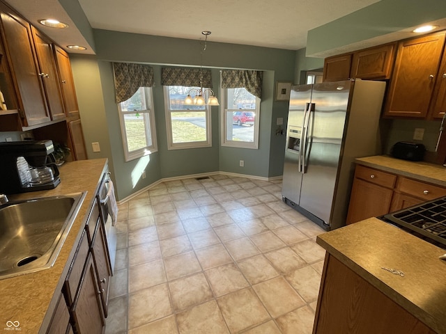 kitchen featuring baseboards, stainless steel fridge with ice dispenser, decorative light fixtures, brown cabinetry, and a sink