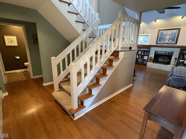 stairway with a brick fireplace, baseboards, vaulted ceiling, wood finished floors, and a ceiling fan