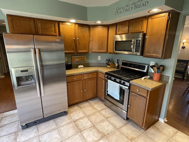 kitchen with stainless steel appliances, brown cabinetry, and light countertops