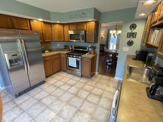 kitchen with brown cabinets, a sink, appliances with stainless steel finishes, light countertops, and a chandelier