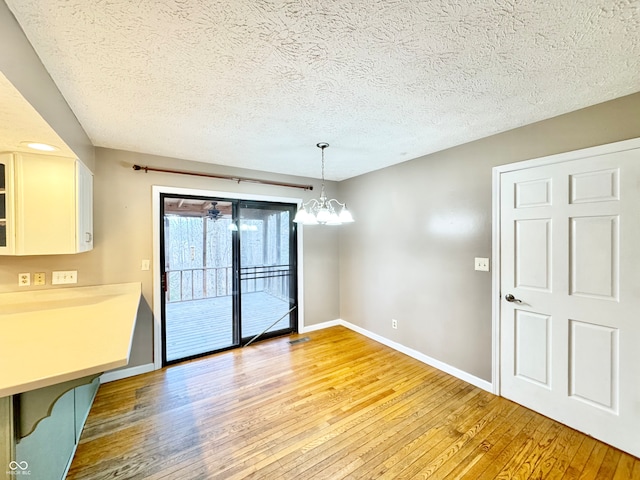 unfurnished dining area featuring light wood-style floors, a chandelier, a textured ceiling, and baseboards