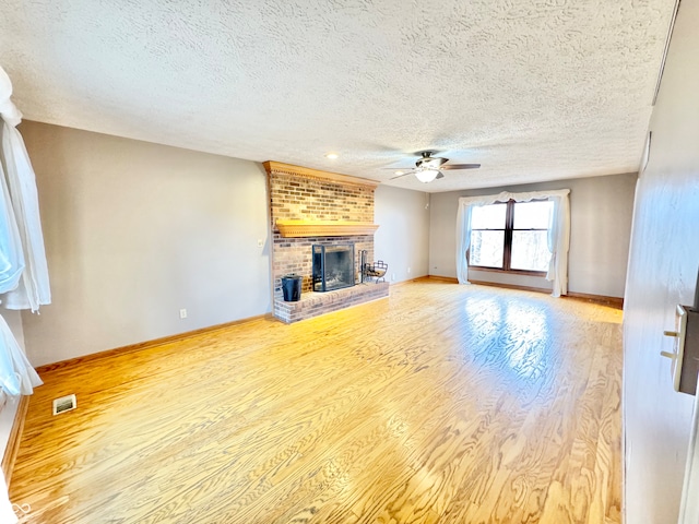 unfurnished living room featuring visible vents, baseboards, a ceiling fan, wood finished floors, and a brick fireplace