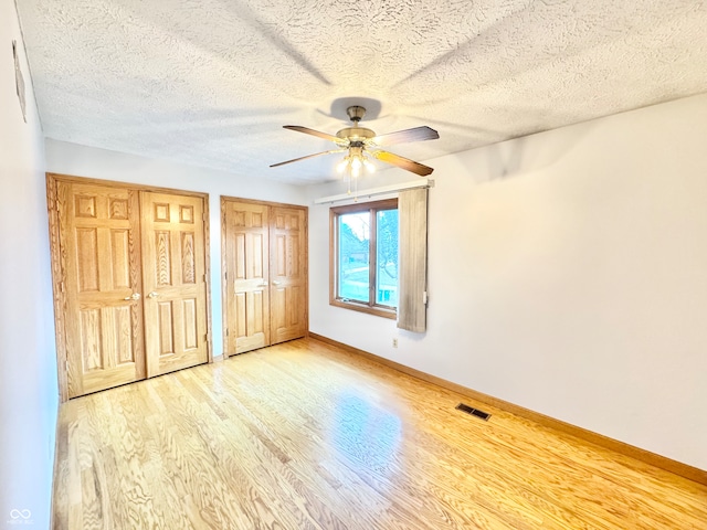 unfurnished bedroom with ceiling fan, wood finished floors, visible vents, baseboards, and two closets