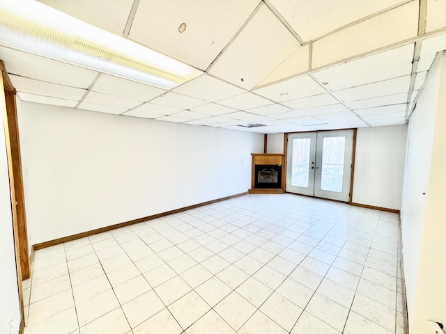 below grade area featuring french doors, a fireplace, a paneled ceiling, and baseboards