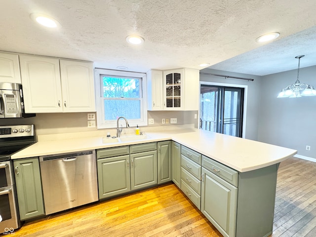 kitchen featuring stainless steel appliances, a sink, a peninsula, and light wood finished floors