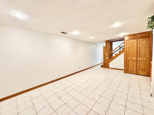 finished below grade area featuring baseboards, visible vents, stairway, and a textured ceiling