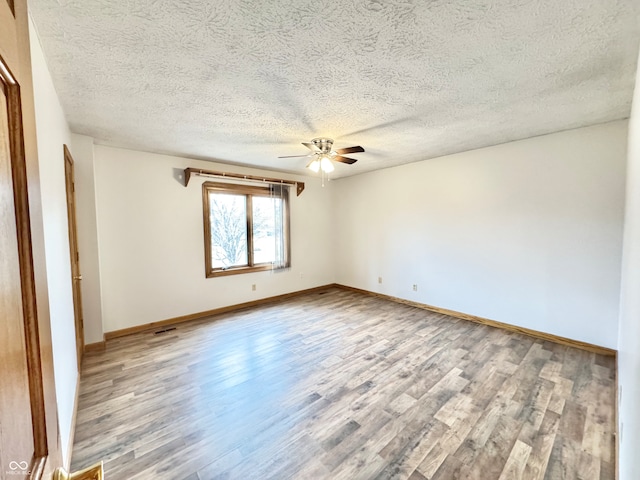 empty room with ceiling fan, a textured ceiling, baseboards, and wood finished floors