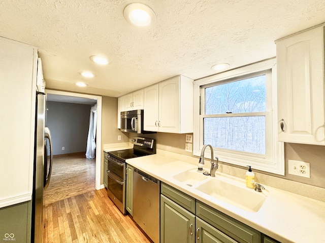 kitchen with light wood-style flooring, appliances with stainless steel finishes, a textured ceiling, white cabinetry, and a sink