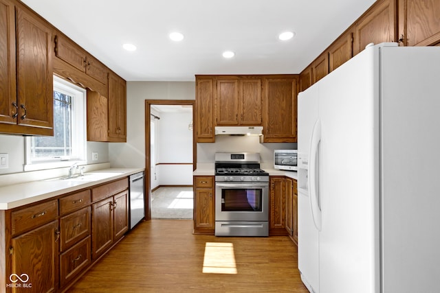 kitchen with light wood-style flooring, stainless steel appliances, light countertops, under cabinet range hood, and a sink