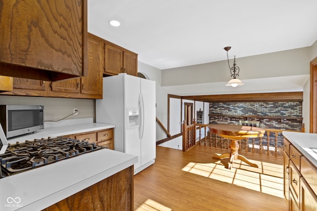 kitchen featuring white refrigerator with ice dispenser, light countertops, light wood-type flooring, brown cabinets, and stainless steel microwave