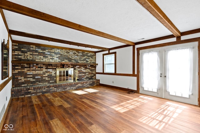 unfurnished living room featuring a textured ceiling, wood finished floors, french doors, a brick fireplace, and beam ceiling