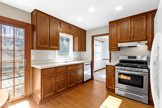 kitchen with under cabinet range hood, a sink, light countertops, appliances with stainless steel finishes, and light wood-type flooring