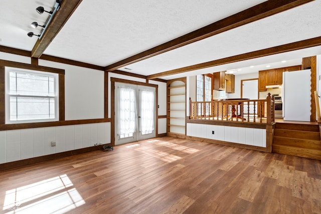 unfurnished living room featuring beam ceiling, a textured ceiling, french doors, and wood finished floors