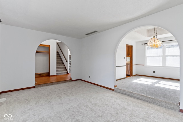 empty room with arched walkways, carpet flooring, visible vents, and baseboards