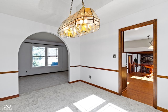 carpeted empty room with arched walkways, lofted ceiling, baseboards, and an inviting chandelier