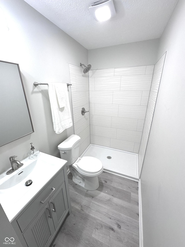 full bathroom featuring toilet, a textured ceiling, vanity, wood finished floors, and tiled shower