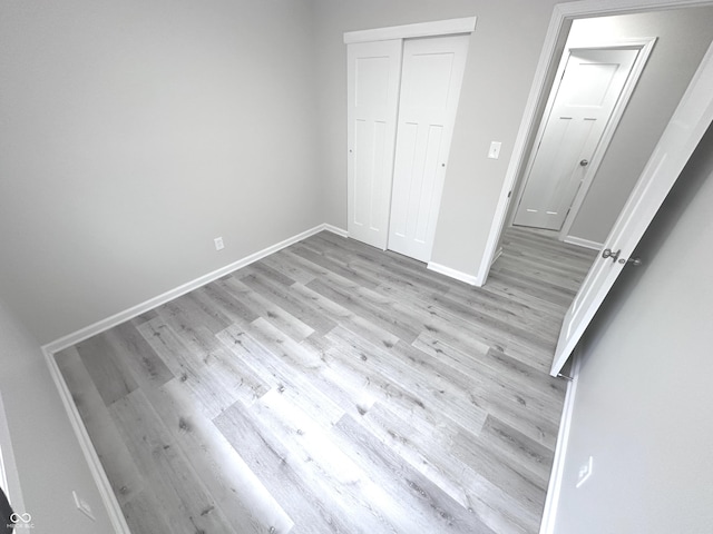 unfurnished bedroom featuring light wood-type flooring, baseboards, and a closet