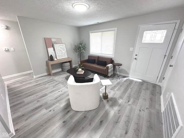 living area featuring baseboards, visible vents, light wood-style flooring, and a textured ceiling